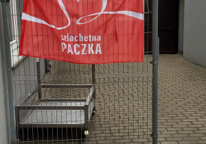 Flaga z logo Szlachetnej Paczki wisi na bramie magazynu, miejscu zbiórki paczek.