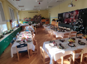 Ustawione stoły w sali przedszkolnej, przygotowane do wspólnego, świątecznego obiadu.