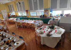 Przystrojone stoły, ustawione w sali przedszkolnej, przygotowane do wspólnego, świątecznego obiadu.