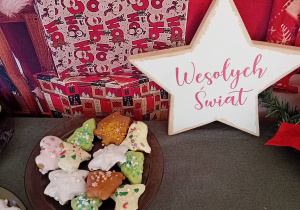 Pierniki leżą na talerzu na tle dekoracji świątecznej - gwiazdki z napisem "Wesołych świąt".