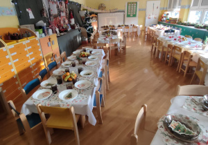 Przystrojone stoły, ustawione w sali przedszkolnej, przygotowane do wspólnego, świątecznego obiadu.