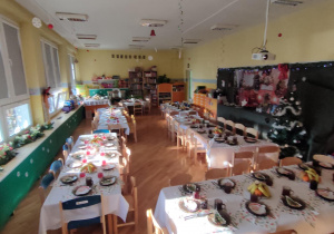 Przystrojone stoły, ustawione w sali przedszkolnej, przygotowane do wspólnego, świątecznego obiadu.