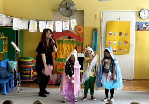 Troje dzieci przebrane za postaci z Lodowej Krainy tańczą z panią Natalią na środku sali, przed nimi siedzą pozostałe dzieci.