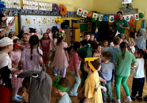 Dzieci, przebrane w wiosenne stroje tańczą w sali.