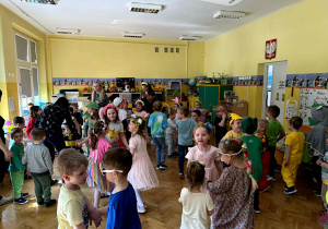 Dzieci, przebrane w wiosenne stroje tańczą w sali.