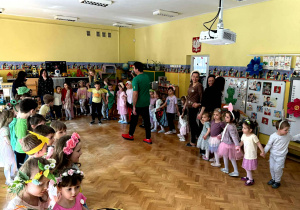 Dzieci, przebrane w wiosenne stroje tańczą w sali w kółku.