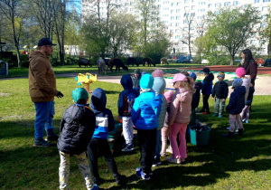 Dzieci stoją w grodzie przedszkolnym, słuchają prowadzącego ożyciu alpak.