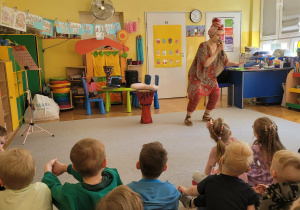 Pani Nutka stoi przed dziećmi, śpiewając piosenkę.