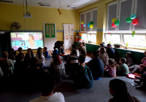 Dzieci wraz z rodzicami siedzą na dywanie w trakcie wiosennego seansu filmowego.