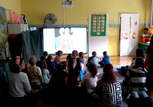 Dzieci wraz z rodzicami siedzą na dywanie w trakcie wiosennego seansu filmowego.