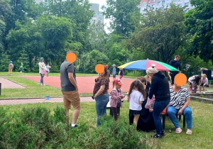 Rodzice z dziećmi w ogrodzie przedszkolnym na pikniku rodzinnym.