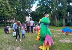 Rodzice z dziećmi w ogrodzie przedszkolnym na pikniku rodzinnym, obok postać papugi, maskotki.