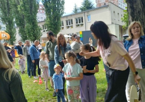 Rodzice z dziećmi w ogrodzie przedszkolnym na pikniku rodzinnym przy stanowisku aktywności sportowych.