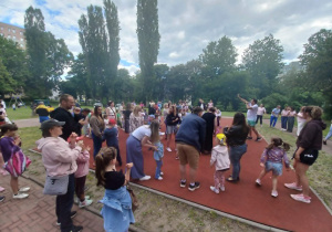 Zabawy muzyczne, w których uczestniczą rodzice z dziećmi na boisku przedszkolym.