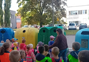 Dzieci zgromadzone przed pojemnikami do segregacji śmieci.