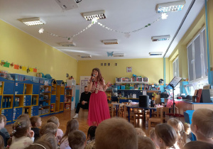 Pani "Nutka" śpiewa dla dzieci, stojąc na środku sali.