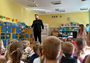 Zaproszony gość śpiewa dla dzieci basem, stojąc na środku sali.