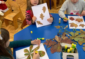 Dzieci naklejają liście na kartony.