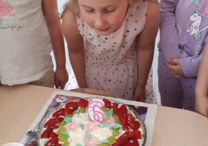 6 urodziny Mai. Maja pochylona nad tortem z zapaloną świeczką.