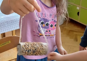 Na zdjęciu widać dziewczynkę przygotowującą kolbę z ziarenek dla ptaszków.
