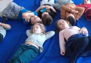 W świecie kosmosu - dzieci leżą na dywanie na plecach, patrząc w sufit, na którym przedstawiona jest imitacja nieba nocą.