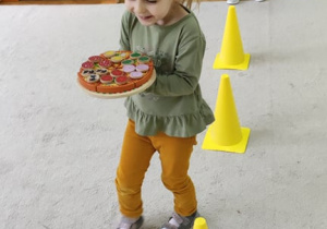 Dzień Pizzy - dzieci bawią się w kelnerów, noszących pizzę wokół żółtych słupków.