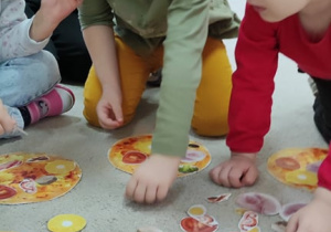 Dzień Pizzy - dzieci siedzą na dywanie i komponują pizzę z przygotowanych elementów.