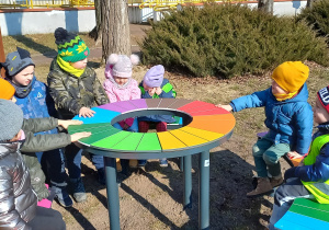 Zabawy dzieci przy tęczowym stoliku w ogródku przedszkolnym.
